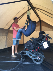 A father hoisting his son from his wheelchair across a beam in a tent.