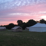 Matching beige tents and a white marque on a field with a crimson sunrise.