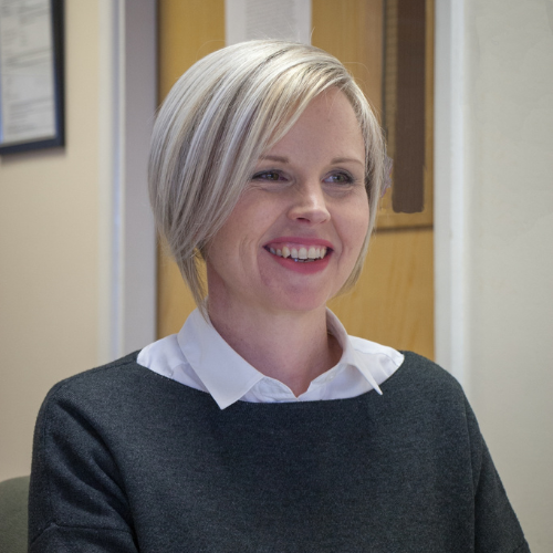 Remarkable white woman and fabulous 24-hour postural care trainer with cropped silver/blond hair wearing a black top and smiling