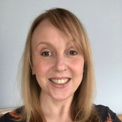 Remarkable white woman and fabulous 24-hour postural care trainer with cropped silver/blond hair wearing a black top and smiling