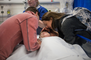 Mother and father leaning over their son in a hospital bed
