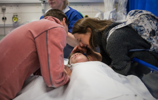 Mother and father leaning over their son in a hospital bed